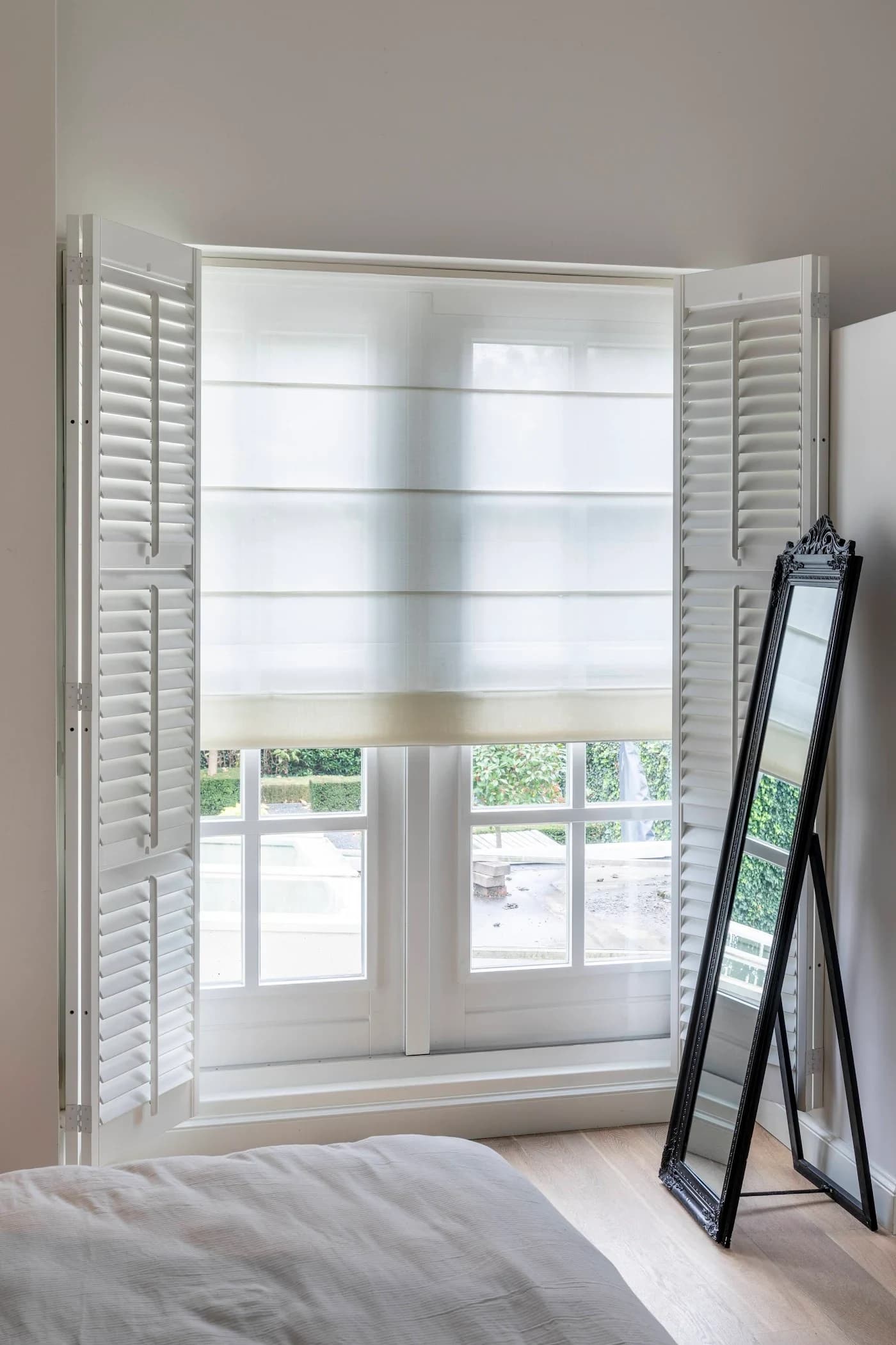 Witte shutters met vouwgordijn in een lichte slaapkamer